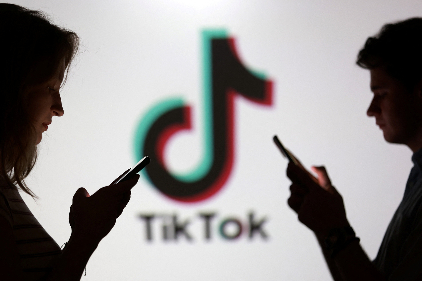 People pose for a photo while holding smartphones in front of the TikTok logo on Sept. 11, 2025. [REUTERS/YONHAP]