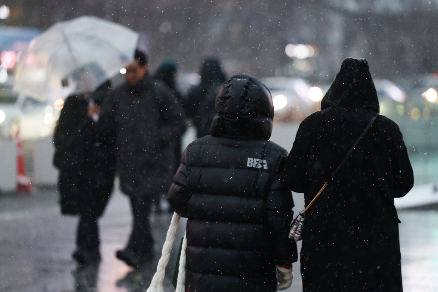 People walk through Gwanghwamun Square in Jongno District, central Seoul, using hoods as it snows on Jan. 12. [YONHAP]