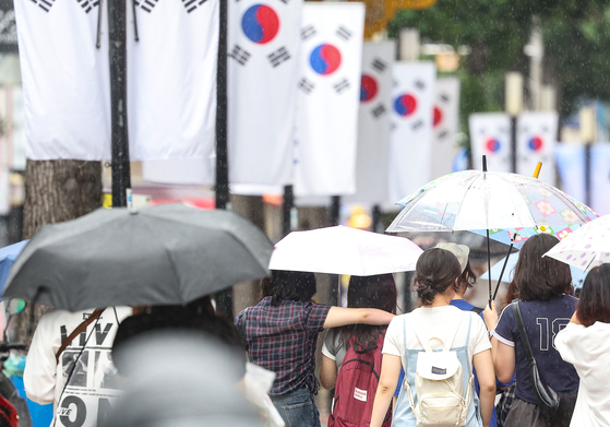 People walk with umbrellas in Daegu, on Aug. 12, 2025, as rain falls and Korean flags are displayed. [YONHAP]