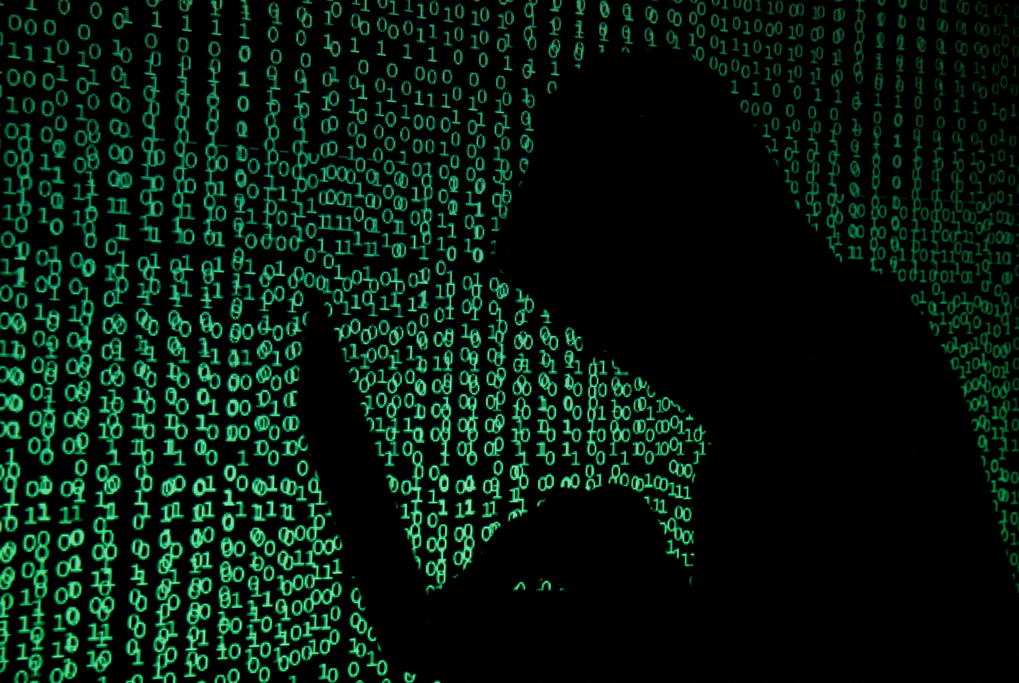 A hooded man holds a laptop computer as cyber code is projected on him in this illustration picture taken on May 13, 2017. [REUTERS/YONHAP]