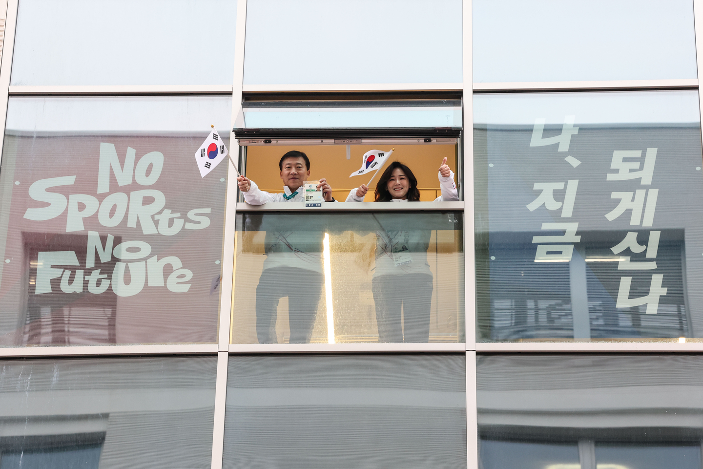 Kim Taek-soo, left, head of the Korean athletes village, and Lee Soo-kyung, chef de mission for Korea at the 2026 Milan-Cortina Winter Olympics, wave the Korean national flag from a window at the Milan Olympic Village in Milan on Feb. 3, three days ahead of the opening of the 2026 Milan-Cortina Winter Olympics. [KIM JONG-HO]