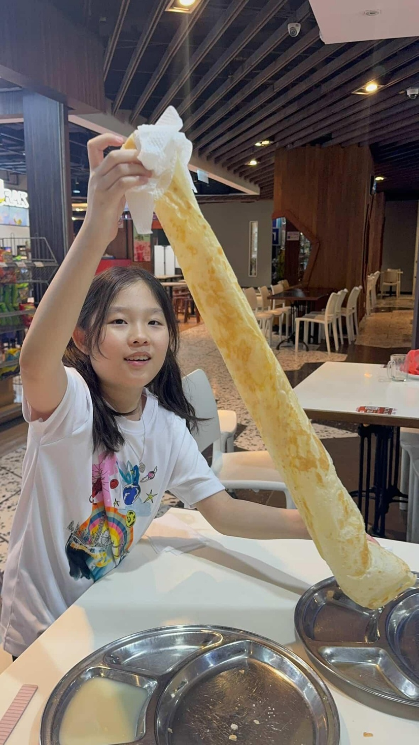 Park Chan-mi’s daughter tries eating Roti tissue, a popular, paper-thin and crispy Malaysian sweet flatbread, at NZ Curry House, a local restaurant in Kuala Lumpur, on Dec. 16, 2025. [PARK CHAN-MI]