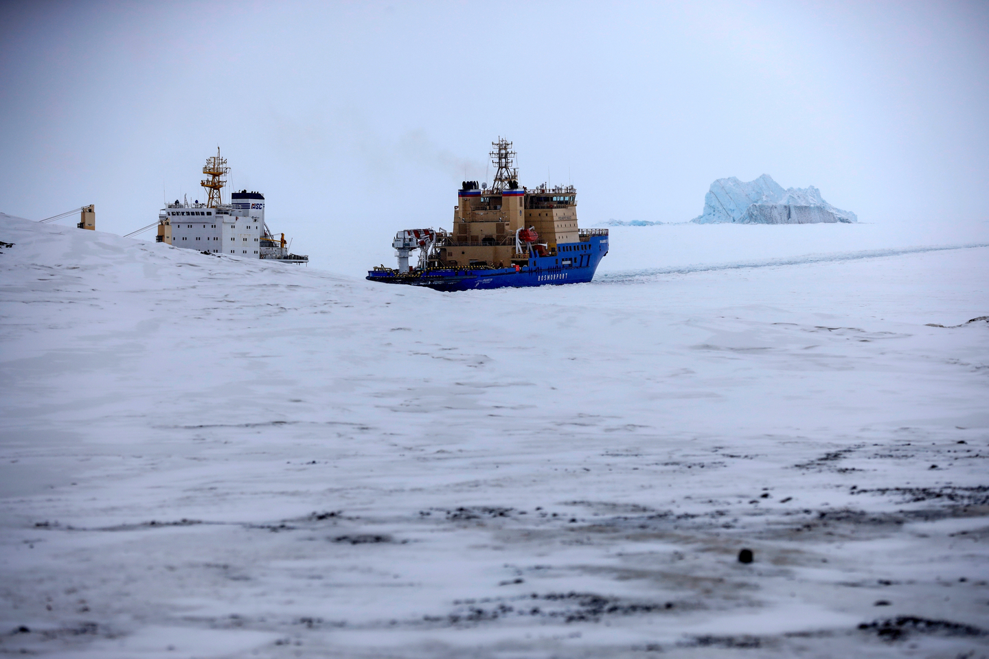 An icebreaker makes the path for a cargo ship with an iceberg in the background near a port on Alexandra Land island near Nagurskoye, Russia, on May 17, 2021.  [AP]