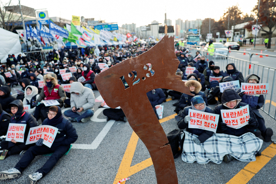Protestors sit near an axe sculpture bearing the date of December 3 during a rally to mark the first anniversary of former President Yoon Suk Yeol's December 3, 2024 martial law declaration, in front of the National Assembly in Yeouido, western Seoul on Dec. 3, 2025. [REUTERS/YONHAP]