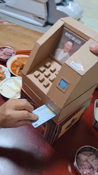 A handmade cardboard ATM spits out a seemingly endless stream of 10,000 won ($7) bills [SCREEN CAPTURE]