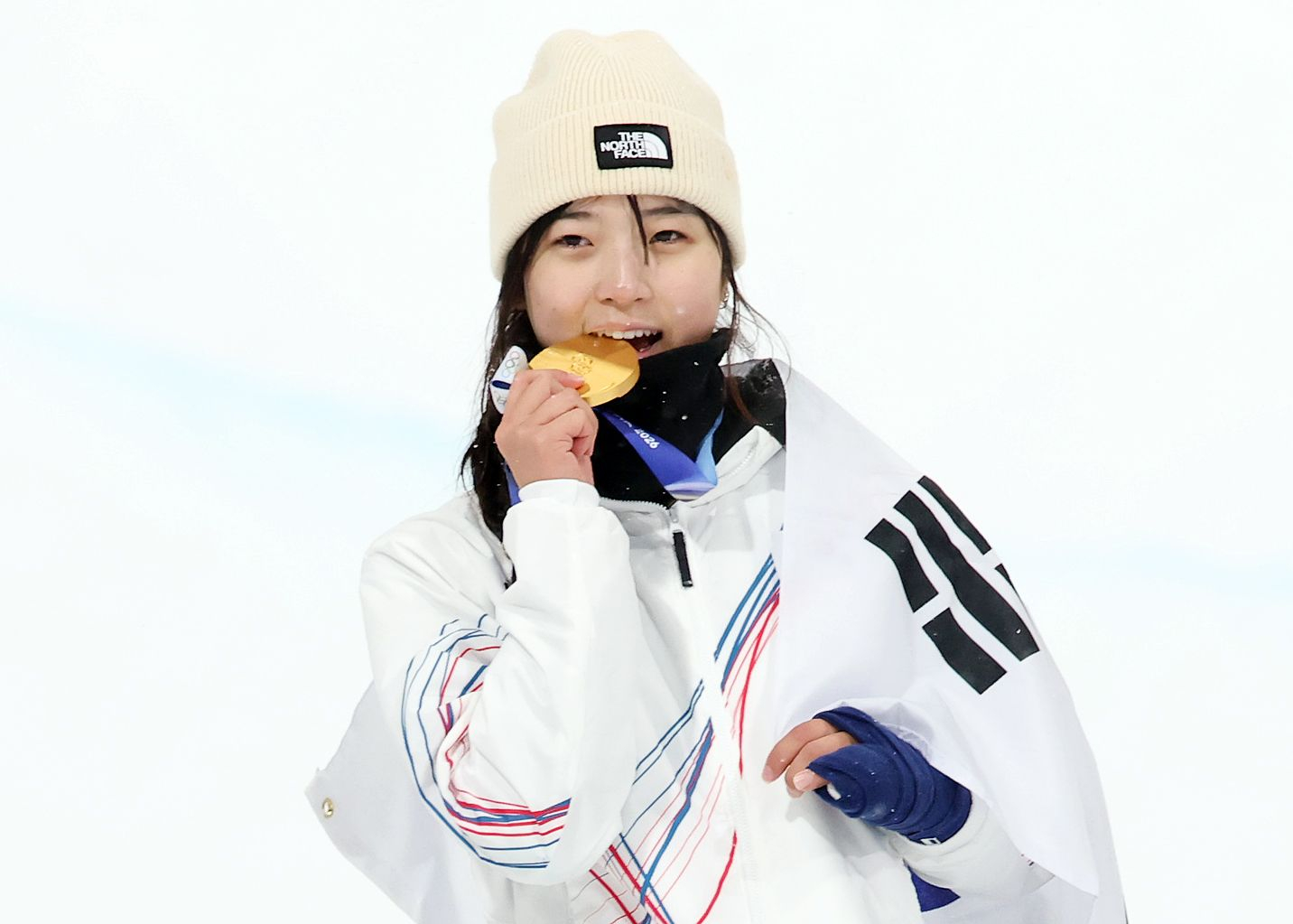 Choi Ga-on of Korea bites down on the gold medal in the women’s snowboard halfpipe final at the 2026 Milan-Cortina Winter Olympics on Feb. 12. [NEWS1]