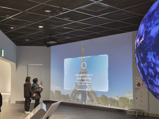 A mother and her son pose for a photo in front of a screen displaying the Eiffel Tower at the Seoul Gallery in the basement of the City Hall in central Seoul on Feb. 11. [CHO JUNG-WOO]