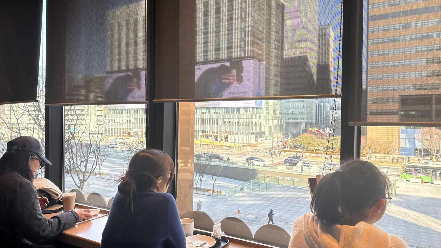 People are seated at the window seats on the third floor of the Starbucks Gwanghwamun branch.