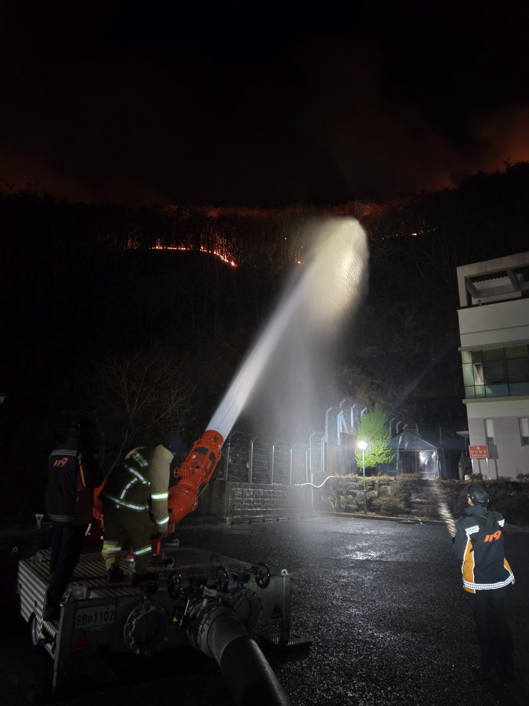 Fire authorities use a high-capacity water cannon system to block flames approaching a nursing hospital as a wildfire that broke out in the afternoon of Feb. 23 in Samnangjin-eup, Miryang, South Gyeongsang, continues for a second day. [GYEONGSANGNAM-DO FIRE DEPARTMENT]