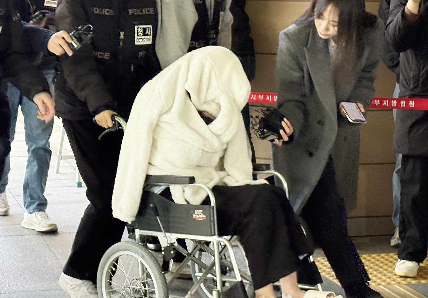 A woman suspected of being under the influence of drugs while driving a Porsche on Banpo Bridge and plunging it onto the Han River riverside, appears for a pre-arrest warrant hearing at the Seoul Western District Court in Mapo District, western Seoul, on Feb. 27, covering her face with a blanket while seated in a wheelchair. [NEWS1]