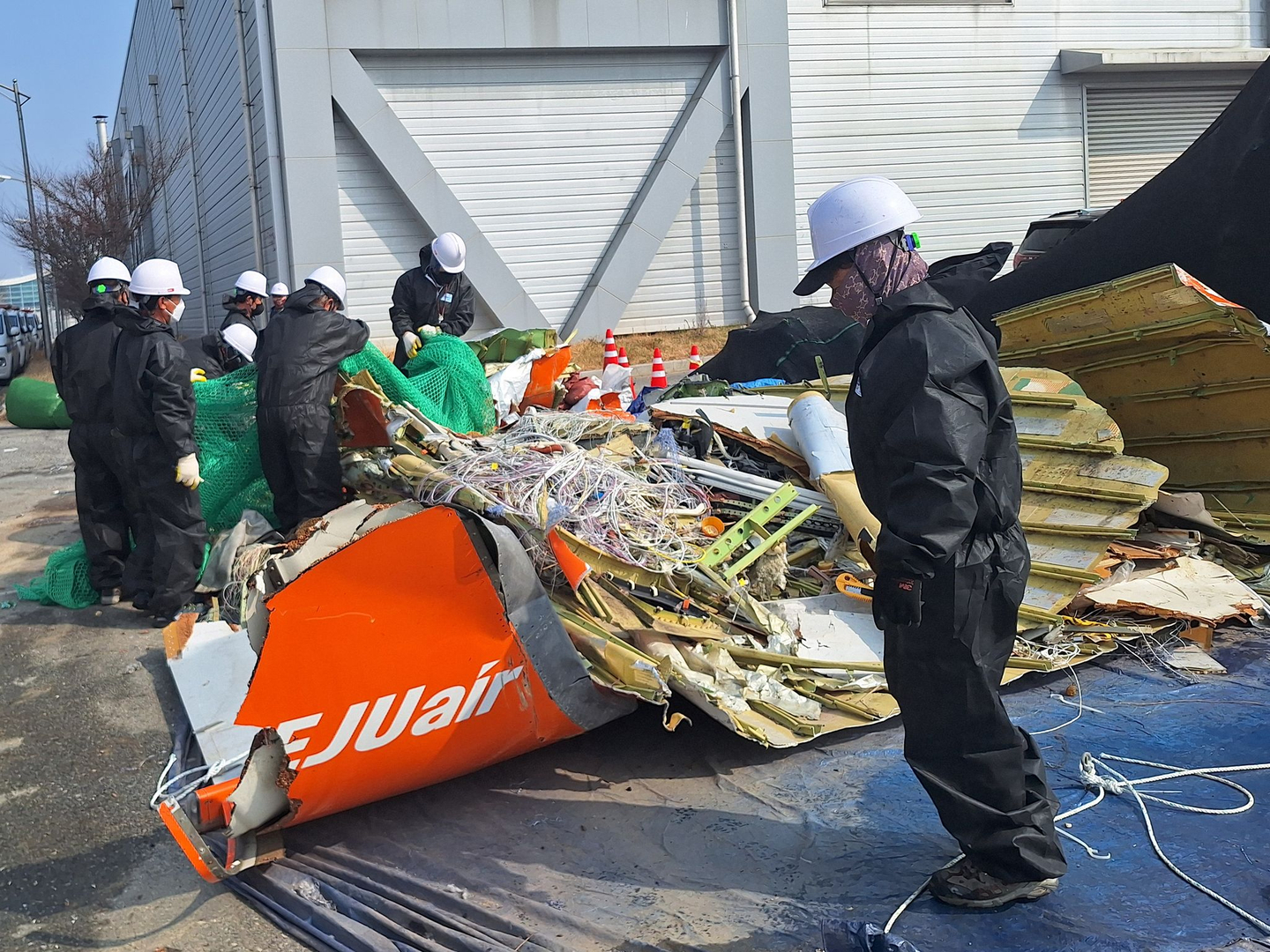 Officials from the Ministry of Land, Infrastructure and Transport, the Aviation and Railway Accident Investigation Board and the scientific investigation unit of the Jeonnam Provincial Police Agency inspect the Jeju Air plane crash wreckage stored behind the airport fire station at Muan International Airport on March 12. [BEREAVED FAMILIES ASSOCIATION FOR THE JEJU AIR PASSENGER PLANE DISASTER AT MUAN INTERNATIONAL AIRPORT]