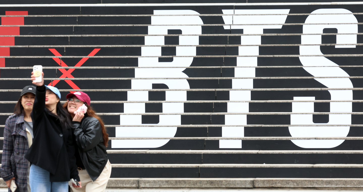 Tourists take a photo in front of a promotional display for BTS’s comeback live performance set up on the steps of the Sejong Center for the Performing Arts in Jongno District, central Seoul, on March 15. [NEWS1] 