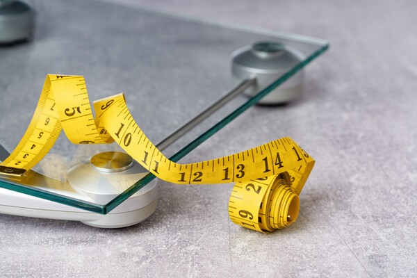 A yellow tape measure lies on top of a glass weighing scale. [GETTY IMAGES BANK]