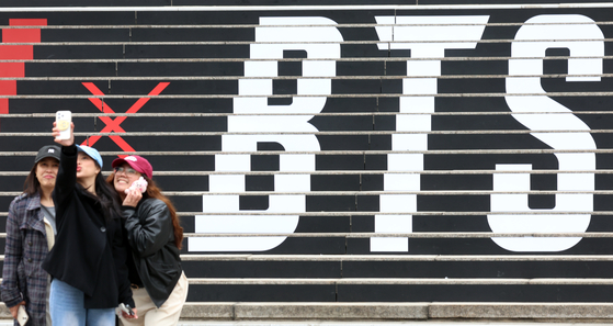 Tourists take a photo in front of a promotional display for BTS’s comeback live performance set up on the steps of the Sejong Center for the Performing Arts in Jongno District, central Seoul, on March 15. [NEWS1] 