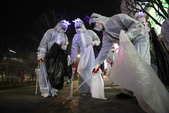 Volunteers wearing hair accessories symbolizing boy band BTS pick up garbage after the group's comeback performance at Gwanghwamun Square in central Seoul on March 21. [YONHAP] 