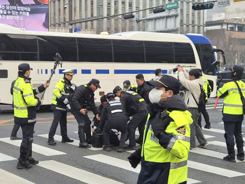 Police restrain a member of the Solidarity Against Disability Discrimination who came to protest at a bus station near Gwanghwamun in Jongno District, central Seoul, on March 27. [YONHAP] 