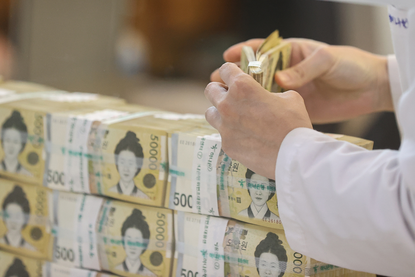 A person counts Korean 50,000-won bills stacked inside a bank in Seoul on Oct. 24, 2022. [YONHAP]