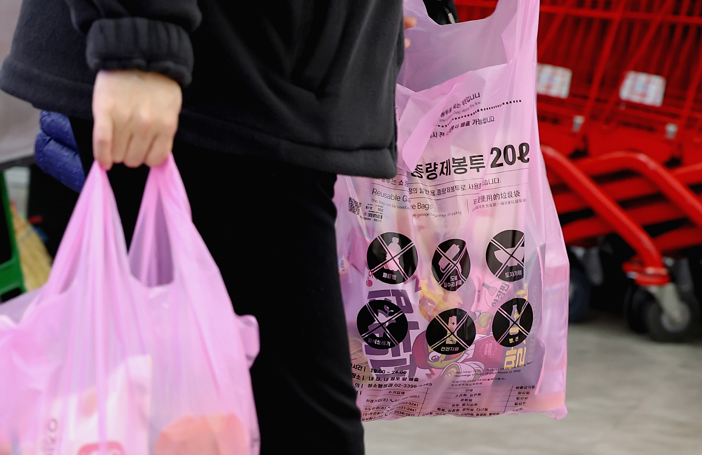 A customer carries groceries in garbage bags, which are offered for bagging to be repurposed for trash disposal later, at a discount store in downtown Seoul on March 30. [NEWS1]