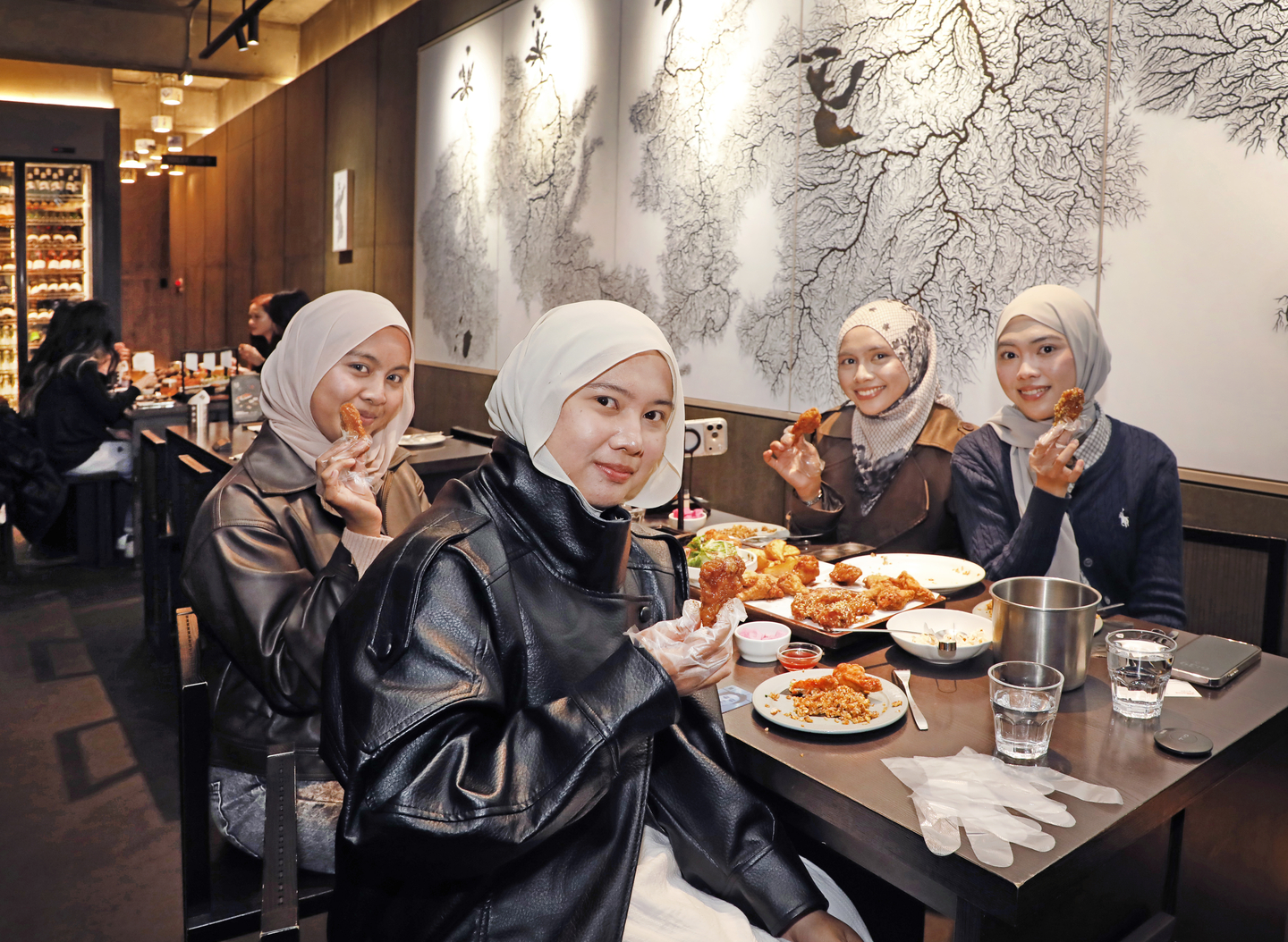 A group of tourists from Malaysia poses in front of the "hanji" (Korean traditional paper) painting on the wall in Kyochon Pilbang, the flagship store of one of Korea's biggest chicken franchises, in Itaewon, central Seoul, on April 7. [PARK SANG-MOON]