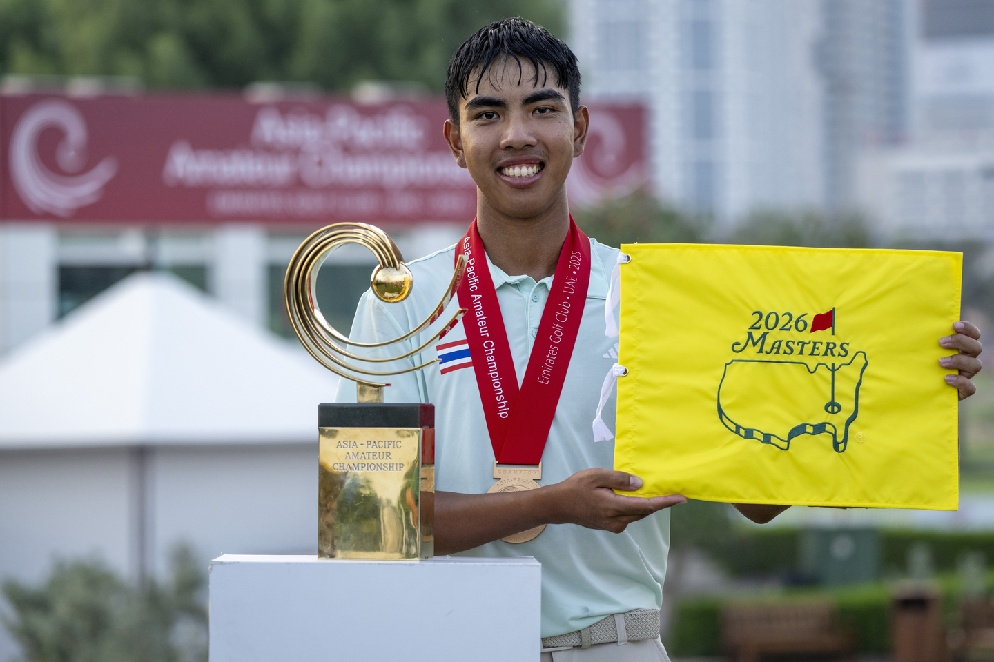 Pongsapak Laopakdee of Thailand lifts the 2026 Masters flag alongside the Asia-Pacific Amateur Championship trophy after winning the tournament following a play-off at the Emirates Golf Club Majlis Course in Dubai, United Arab Emirates, on Sunday, Oct. 26, 2025. [AAC]