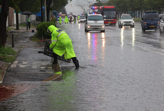 A police officer clears a storm drain cover by hand to prevent road flooding on Jungbong-daero in Seo District, Incheon, on September 17, 2025. [YONHAP] 