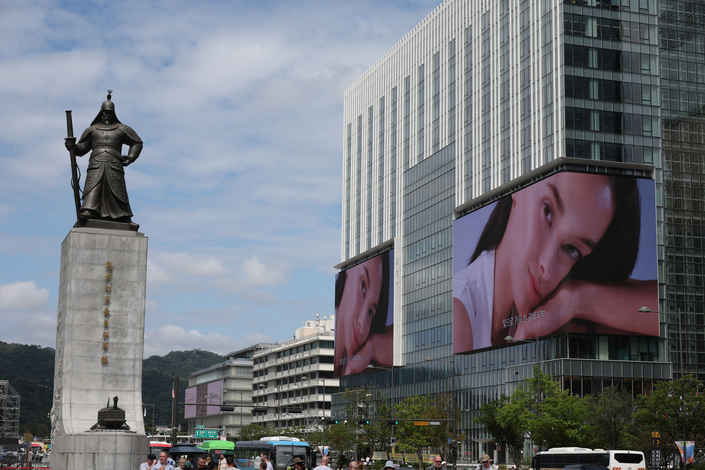 Large digital billboards, right, display an advertisement at KT Gwanghwamun West Building in Jongno District, central Seoul, across the statue of Admiral Yi Sun-sin on Sept. 9, 2025. [YONHAP] 