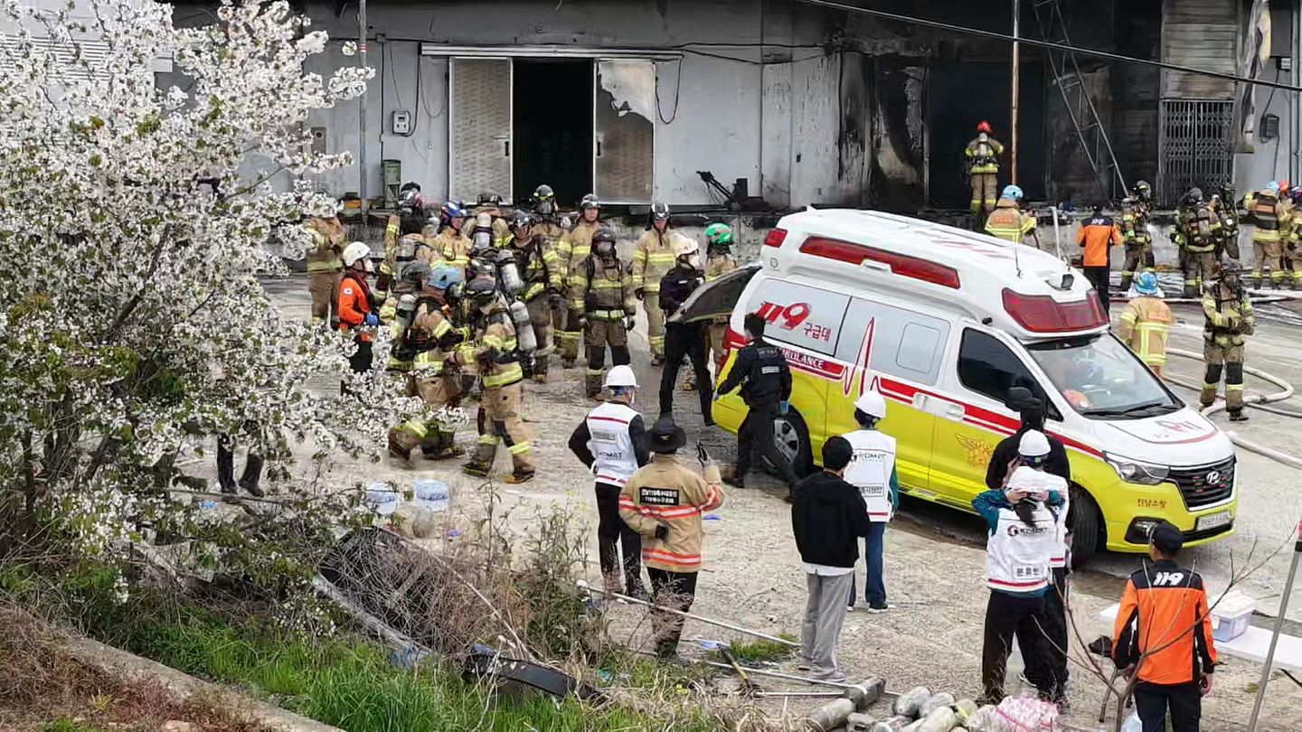 Firefighters watch their colleagues' bodies being moved into an ambulance after they were found dead inside a warehouse in Wando County, South Jeolla, on April 12. [YONHAP]
