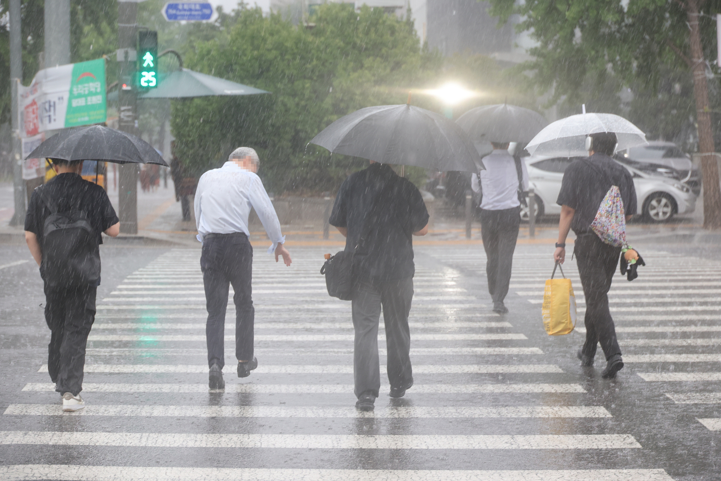 People walk on a crosswalk in rain in western Seoul in July 2025. [YONHAP] 