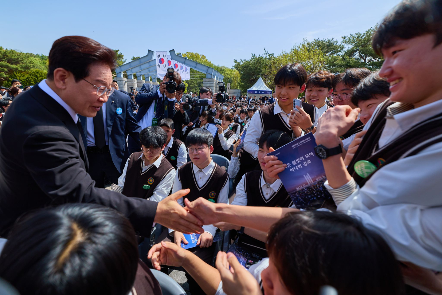 President Lee Jae Myung, left, shakes hands with students after a ceremony to mark the 66th anniversary of the 1960 pro-democracy uprising at the April 19th National Cemetery in Seoul on April 19. [BLUE HOUSE]