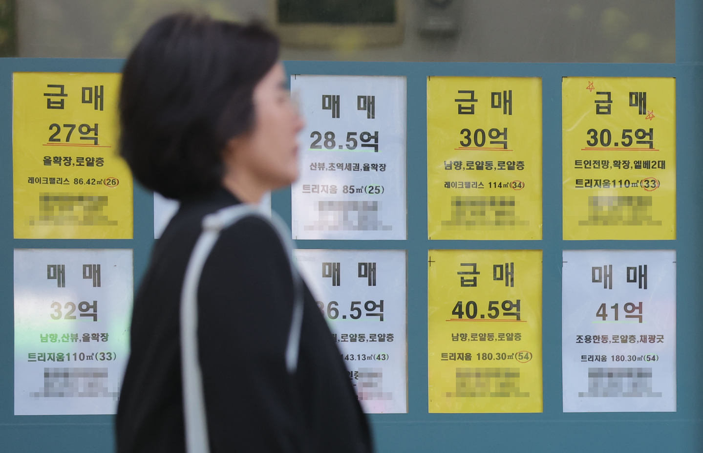 A woman walks by a real estate agency in Seoul with listings displayed on its window on April 16. [YONHAP]