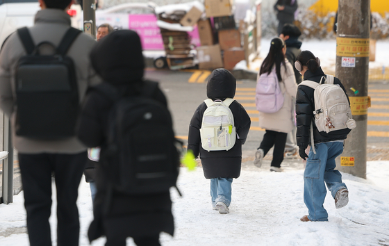 Children walk on snow-covered streets near an elementary school in western Seoul in February. [YONHAP]