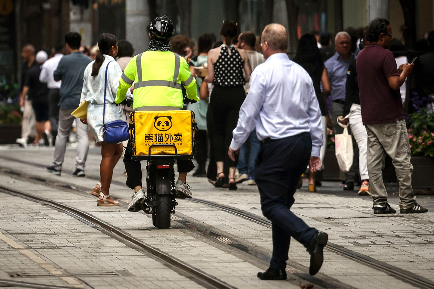 Pedestrians walk past a HungryPanda food delivery rider in central Sydney, Australia, on Feb. 19. [AFP/YONHAP]